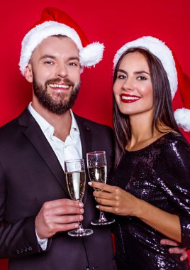 Bir güzel yeni yıl ve Noel var. Neşeli güzel gülümseyen birkaç bardak şampanya topları ile kırmızı bir arka plan ile Noel Baba şapkaları severler. Tatil severler