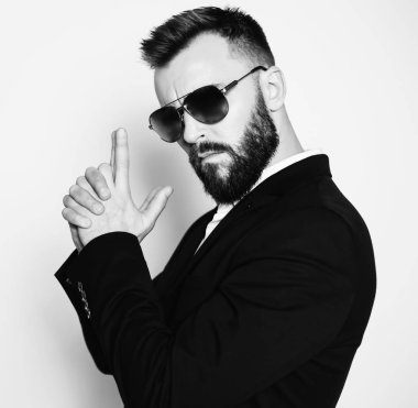 Zarif siyah bir takım elbise ve siyah gözlük bağı poz içinde ayakta acımasız yakışıklı, sakallı adam.