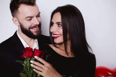 Güzel mutlu gülümseyen çifte sarılma ve ellerinde çiçeklerle kameraya bakarak şık kostümleri aşık.