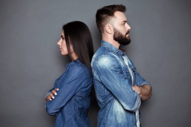 Ciddi erkek ve kadın arka arkaya izole gri bir arka plan karşı rahat kıyafet içinde duruyorsun.