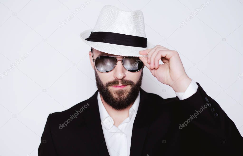 Elegant macho. Handsome young stylish bearded man in hat and sunglasses looking directly at the camera on a white background isolated.