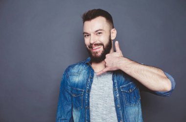 Sizi geri arayalım. Kot gömlek gülümseyen güzel modern insan el telefon gösterir ve onun kulağı gri bir arka plan üzerine koyar.