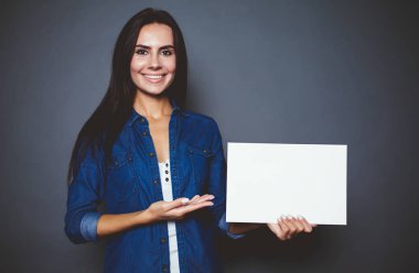 Eller izole gri arka plan üzerinde reklam için boş sayfa ile bir kot gömlek güzel modern gülümseyen kadın.