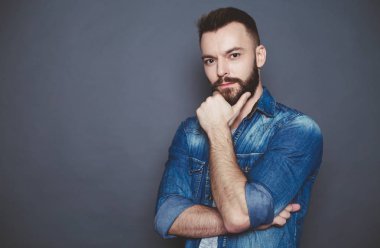 Gri bir arka planda geçti silah ile bir denim tişörtlü adam yakışıklı düşünceli genç sakallı.