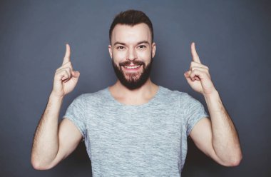 Bu ne ihtiyaç vardır. Yakışıklı genç gülümseyen adam gri arka plan Puan parmakları kendini sakallı.