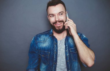 Merhaba tatlım. Modern çekici gülümseyen bir adam bir kot gömlek eşiyle telefonda gri bir arka plan üzerinde konuşuyor.