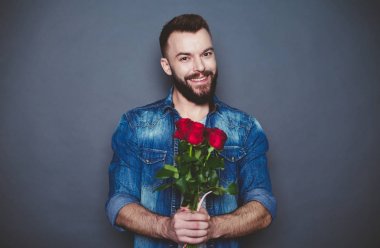 Sevgili hediyesi. Gülümseyen güzel bir kot gömlekli sakallı adam gri bir arka plan üzerinde kırmızı gül tutan.