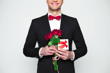 Şık gülümseyen yakışıklı modern insan resmi siyah takım elbise ve kırmızı papyon hediye kutusu ve güzel kırmızı gül elinde tutuyor. Arkadaş sevgili kadın için Hediyelik.