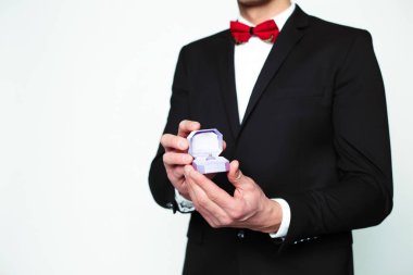 Yakışıklı gülümseyen modern zarif insan resmi siyah takım elbise ve kırmızı papyon bir nişan yüzüğü ile bir kutu koruyor ve kamera gösterir.