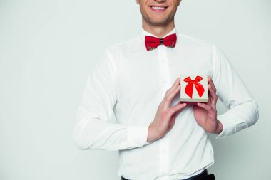 Sevgili için bir hediye. Genç güzel bir beyaz gömlek ve kırmızı bir kutu bir hediye ile tutarak papyon zarif erkekte gülümseyen ve kameraya gösterir. Sevgililer günü.