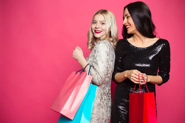 购物理念 购物的女孩朋友 两个开朗美丽的微笑的妇女与购物袋在粉红色的背景 — 图库照片