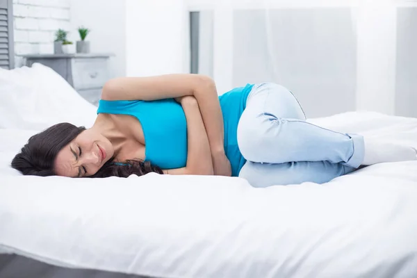 女性の痛みや月経症候群 自宅ベッドの上で横になっている若い女性彼女の胃の上に保持し カールのけいれん — ストック写真