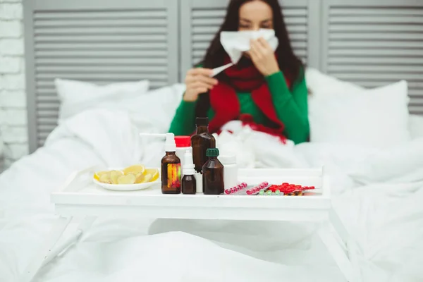 Very high body temperature. A young sick woman in a red scarf measures the temperature with a thermometer. The concept of health and disease.