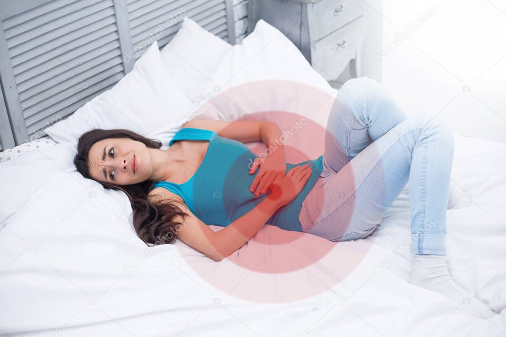 Women's pain or menstrual syndrome. A young woman lying on a bed at home holds onto her stomach and curls through spasms.
