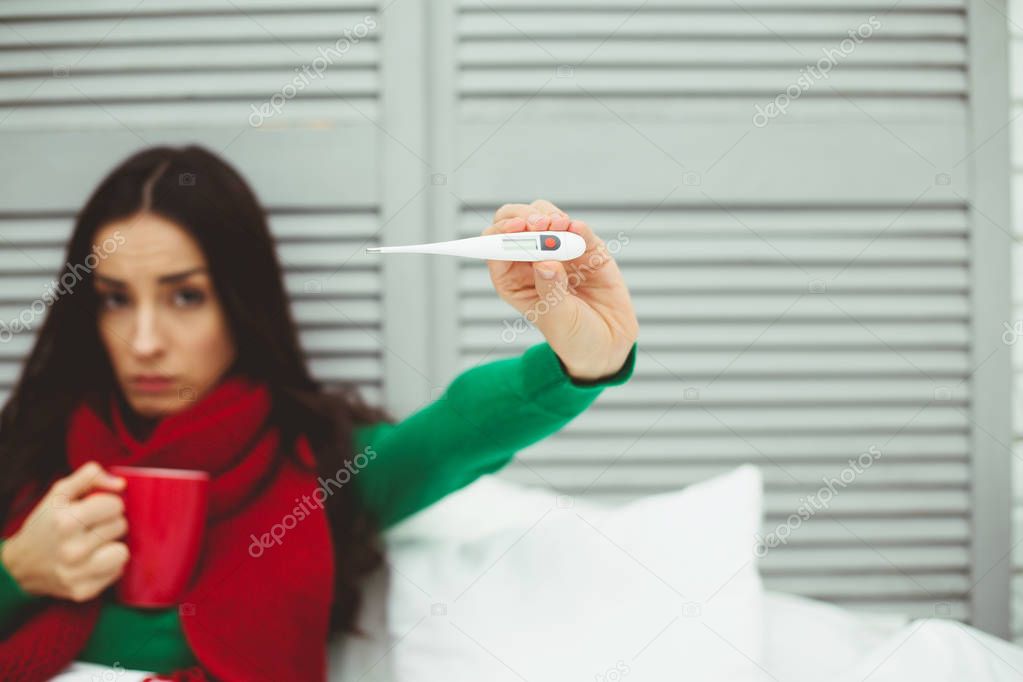 Very high body temperature. A young sick woman in a red scarf measures the temperature with a thermometer. The concept of health and disease.