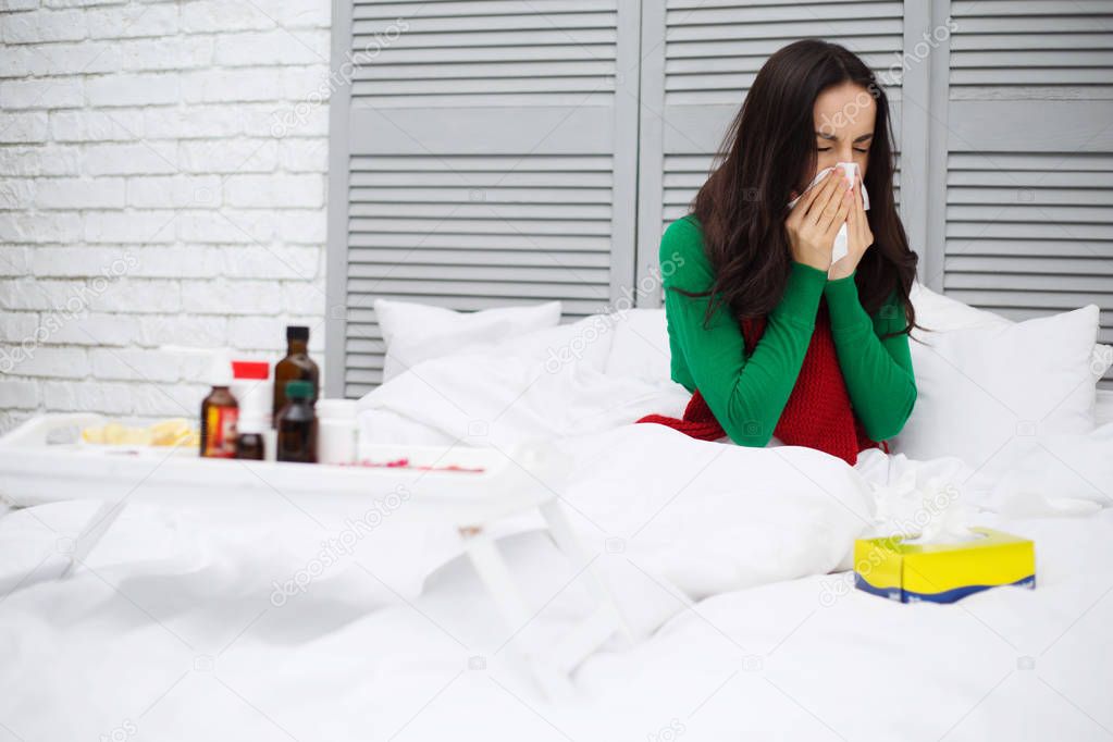 Close up portrait of a young sick woman with a runny nose in a red scarf lying on the bed at home and treated. The concept of health and disease.