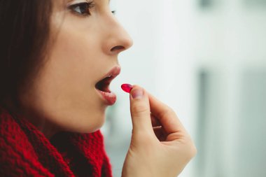 İlaç kullanıyor. Bir hap ağzına getiren genç bir hasta kadının fotoğrafını kapatın.