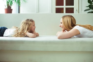 Anneler ve kızları. Genç güzel kadın ve küçük bir sarışın kız beyaz kanepede yüz yüze yalan ve birbirinize bakın.