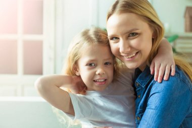 Gülümseyen ve mutlu anne ve kızı evde birbirinizi kanepede sarılıyorlar. Anne ve kızı iyi eğlenceler. 