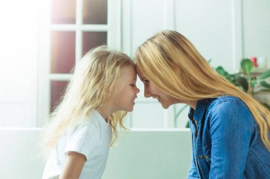 Gülümseyen güzel sarışın anne ve kızı alınlarına birbirlerine evde kanepede oturan dokun. Anneler günü. Kadınlar Günü. 8 Mart.