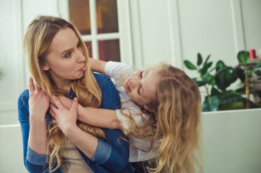 Gülümseyen ve mutlu anne ve kızı evde birbirinizi kanepede sarılıyorlar. Anne ve kızı iyi eğlenceler. 
