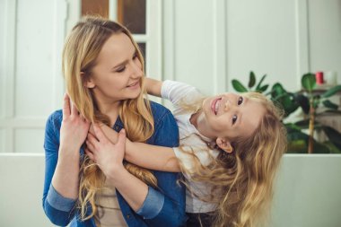 Gülümseyen ve mutlu anne ve kızı evde birbirinizi kanepede sarılıyorlar. Anne ve kızı iyi eğlenceler. 