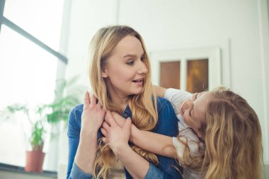Gülümseyen ve mutlu anne ve kızı evde birbirinizi kanepede sarılıyorlar. Anne ve kızı iyi eğlenceler. 