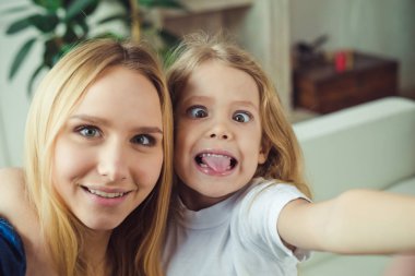 Gülümseyen ve mutlu anne ve kızı evde birbirinizi kanepede sarılıyorlar. Anne ve kızı iyi eğlenceler. 
