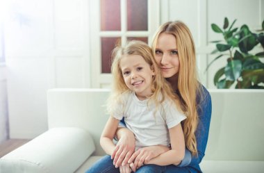Gülümseyen ve mutlu anne ve kızı evde birbirinizi kanepede sarılıyorlar. Anne ve kızı iyi eğlenceler. 
