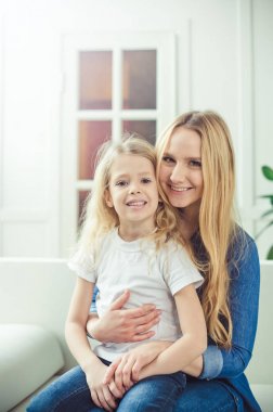 Gülümseyen ve mutlu anne ve kızı evde birbirinizi kanepede sarılıyorlar. Anne ve kızı iyi eğlenceler. 