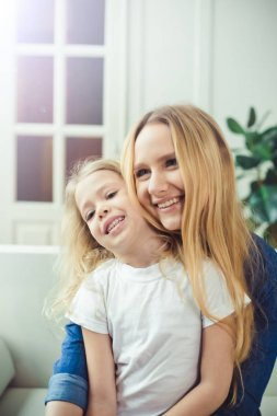 Gülümseyen ve mutlu anne ve kızı evde birbirinizi kanepede sarılıyorlar. Anne ve kızı iyi eğlenceler. 