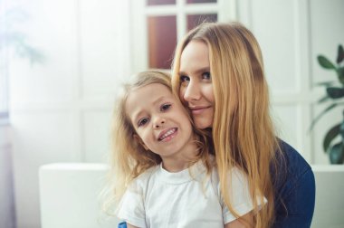 Gülümseyen ve mutlu anne ve kızı evde birbirinizi kanepede sarılıyorlar. Anne ve kızı iyi eğlenceler. 