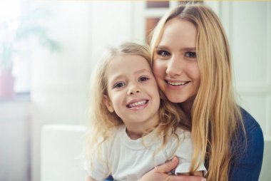 Gülümseyen ve mutlu anne ve kızı evde birbirinizi kanepede sarılıyorlar. Anne ve kızı iyi eğlenceler. 