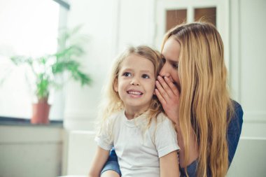 Gülümseyen ve mutlu anne ve kızı evde birbirinizi kanepede sarılıyorlar. Anne ve kızı iyi eğlenceler. 