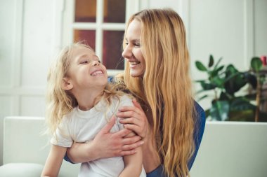 Gülümseyen ve mutlu anne ve kızı evde birbirinizi kanepede sarılıyorlar. Anne ve kızı iyi eğlenceler. 