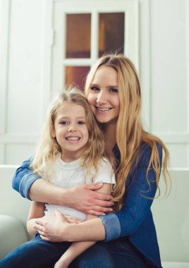 Gülümseyen ve mutlu anne ve kızı evde birbirinizi kanepede sarılıyorlar. Anne ve kızı iyi eğlenceler. 