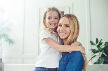 Gülümseyen ve mutlu anne ve kızı evde birbirinizi kanepede sarılıyorlar. Anne ve kızı iyi eğlenceler. 