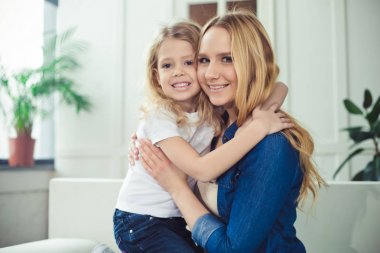 Gülümseyen ve mutlu anne ve kızı evde birbirinizi kanepede sarılıyorlar. Anne ve kızı iyi eğlenceler. 