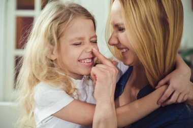 Gülümseyen ve mutlu anne ve kızı evde birbirinizi kanepede sarılıyorlar. Anne ve kızı iyi eğlenceler. 