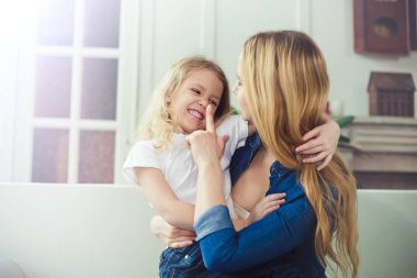 Gülümseyen ve mutlu anne ve kızı evde birbirinizi kanepede sarılıyorlar. Anne ve kızı iyi eğlenceler. 