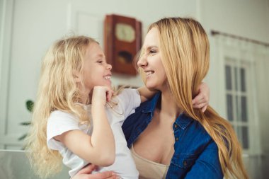 Gülümseyen ve mutlu anne ve kızı evde birbirinizi kanepede sarılıyorlar. Anne ve kızı iyi eğlenceler. 