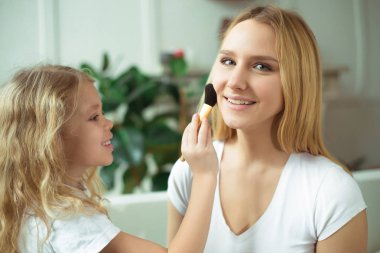 Anne kızını makyaj nasıl öğretir. Güzel gülümseyen sarışın anne ve kızı evde kanepede oturuyorsun. Küçük kız bir fırça toz tutan.