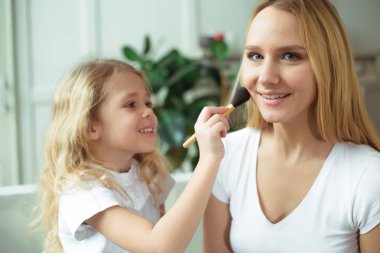 Anne kızını makyaj nasıl öğretir. Güzel gülümseyen sarışın anne ve kızı evde kanepede oturuyorsun. Küçük kız bir fırça toz tutan.