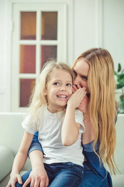 Sana bir sır. Neşeli gülümseyen güzel sarışın anne ve kızı evde kanepede oturan kucaklamak. Anneler günü. Kadınlar Günü. 8 Mart.