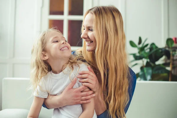 Gülümseyen ve mutlu anne ve kızı evde birbirinizi kanepede sarılıyorlar. Anne ve kızı iyi eğlenceler. 