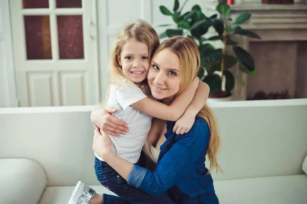 Smiling and happy mom and daughter are hugging each other at home on the couch. Mom and daughter  have fun.