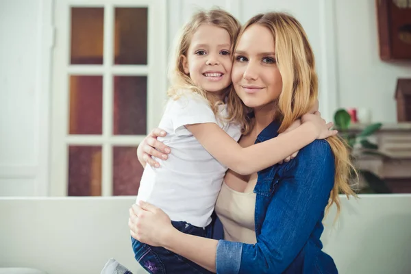 Smiling and happy mom and daughter are hugging each other at home on the couch. Mom and daughter  have fun.