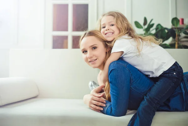 微笑着 快乐的妈妈和女儿在沙发上互相拥抱 妈妈和女儿玩得开心 — 图库照片