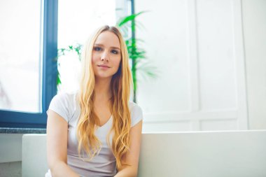 Evde bir kanepede oturan ve dinlenme veya rahatlatıcı bir güzel gülümseyen genç sarışın bir kadın portresi kapatın.