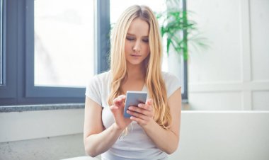 Evde bir telefon ile kanepede oturan güzel genç sarışın bir kadın portresi. Evde sakin ol. Arkadaşlar İnternet ile iletişim